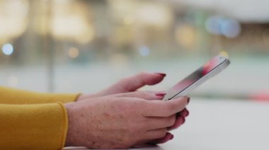 Yakın plan kadın elleri, beyaz tenli, tanınmayan bir kadın telefonda yazıyor. Orta yaşlı iş kadını, e-posta yazma, mesajlaşma iletişimlerini kontrol ediyor. Akıllı telefondaki mesajlar için mobil uygulama kullanıyor.