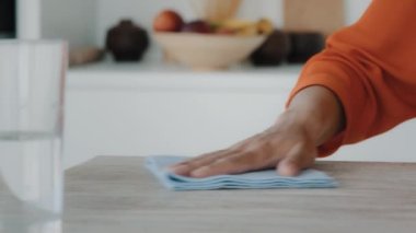 Tanınmayan Afrikalı ev hanımı yemek pişirdikten sonra mutfak yüzeylerini siliyor. Profesyonel kadın ellerini havluyla kapatıyorlar. Cam bardakları su temizleyicisiyle tutuyorlar.