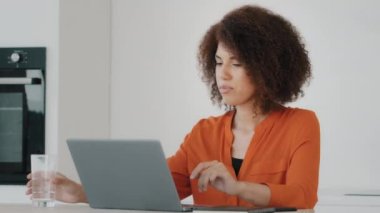 African American businesswoman biracial freelancer worker girl female student in orange blouse working laptop feeling thirsty drinking from glass water balance health care diet refreshment daily habit