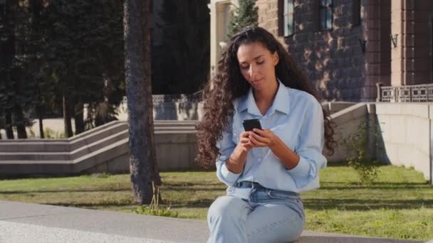 街の通りに座っている若い女の子は スマートフォンでオンラインでチャットを見ている予期せぬ出会い系日に驚くべき手を振って歓迎シンボル招待サイン — ストック動画