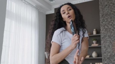 Yakın plan komik, dışavurumcu kadın mikrofon gibi uzaktan kumandayla evde şarkı söylüyor. Mutlu komik kız dans ediyor. Haftasonu kadın blogcu kayıtlarından keyif alıyor.