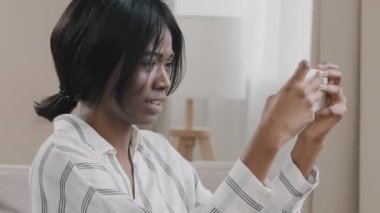 Young excited tense woman gambler holding smartphone looking at screen of phone playing mobile gambling game feels emotional intensity trying to win grimaces using application plays at home on weekend