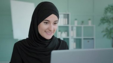 Gülümseyen İslami Arap iş kadını ev ofisinde bilgisayarla çalışıyor. Portre pozitif kadın profesyonel Müslüman yönetici çevrimiçi öğretmen programcı bayan işyerinde daktilo yazıyor