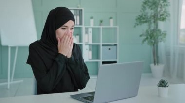 Siyah tesettürlü Müslüman başarılı kadın zaferi kutluyor. Dizüstü bilgisayar ekranına bak. Kapalı ağzı şaşırtan bir piyango teklifiyle şaşırt.