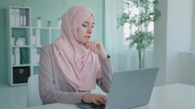 Arap işçi kullanıcısı, Müslüman iş kadını ofiste tesettüre oturmuş dizüstü bilgisayara bakıyor kötü haberler okuyor, işten çıkarılmış postayı okuyor üzgün bir şekilde iflas sorunu inkar ediyor.