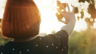 İnsan elini kapat tanınmaz halde kızıl saçlı genç kız yaz güneşinden kısa saçlı güneş ışığı örtüleriyle altın saatinde arka planda gün batımı şehir sokaklarında doğa gökyüzünün tadını çıkarıyor.