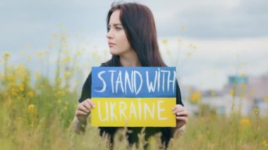 Portrait outdoors profile female face upset woman patriotic girl hold colorful cardboard written inscription stand with Ukraine showing symbolic artwork picture drawing in national blue yellow colors