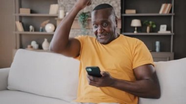 Kıdemli yaşlı Afrikalı erkek kazanan evde cep telefonu uygulaması kullanıyor. Mutlu Amerikalı yetişkin büyükbaba iyi haber mesajı alıyor. İnternet siparişi alıyor, mobil oyun kazanıyor.