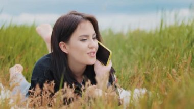 Caucasian young girl woman girlfriend lying on grass green lawn talk mobile phone gossiping tell secret enjoy wireless communication hear good news lovely chatter with boyfriend use internet outdoors