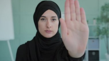 Portrait serious frustrated angry Arabian Muslim Islamic girl in black hijab upset woman looking at camera holding hand in front forbidden gesture refusal stop symbol keep distance no gesture refuse
