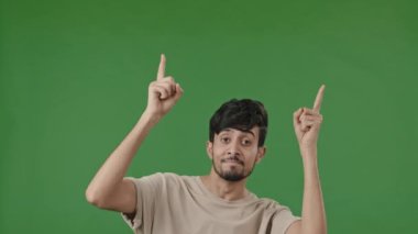 Positive arab man points forefingers up at copy space for advertisement blank place recommends promotional imaginary product pretends shooting pistols choosing make choice isolated on green background
