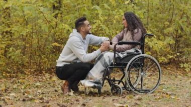 Genç ve mutlu İspanyol çift tatlı tatlı sohbet ediyorlar şefkatli erkek arkadaş, hastane parkındaki hasta kız arkadaşını ziyaret ediyor tekerlekli sandalyedeki kadının rehabilitasyona ihtiyacı var.