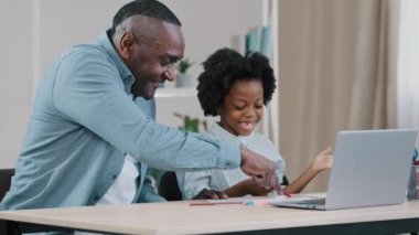 Yetişkin baba, küçük kızına ilkokul ödevini açıklıyor. Sevgi dolu baba, sevimli küçük kıza ev ödevi yaptırıyor. Çocuklara mutlu Afrikalı Amerikan ailesi, evde eğitim kavramını öğretiyor.