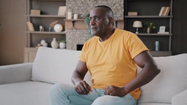 Kıdemli Afro-Amerikan erkeği oturma odasında rahat bir kanepeye oturur uzaktan kumandayı tutar spor programı programı şampiyonluğu yayını dijital televizyon sevinç çığlıkları atar zafer kazanır