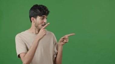 Optimistic humorous portrait arabic man posing in green studio points forefingers aside pretending shooting pistols makes choice thumb up approve good idea advertises promotional product image mockup