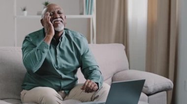 Old bald African business man with gray beard aged male employer sitting on sofa working with laptop feels sudden headache migraine spasm pain holding head suffering from cancer overwork disease ill