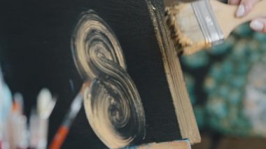 Yakından bir kadın elinin altında fırça izleri, altın rengi çizgiler, siyah arkaplan, tanınmayan kadın ressam, resim çizmekten zevk alıyor.