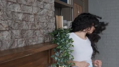 Etkileyici, genç, İspanyol asıllı, komik kadın müziğe ilgi duyuyor, evi temizliyor, neşeli ev hanımı oturma odasında tozunu alıyor, dans ediyor, ritmik dans ediyor, uzun kıvırcık saç temizleme servisi reklamını sallıyor.