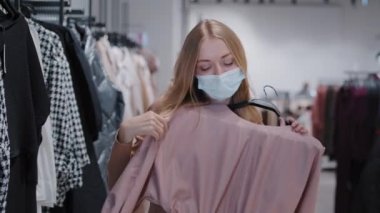 Blonde Caucasian girl in medical mask female client buyer customer woman in covid pandemic shopping mall dancing in cloth store with silk blouse happy with discounts on black friday sweater dance