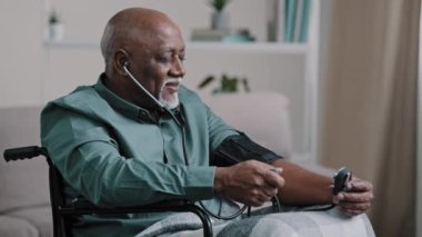 African old man elderly grandfather sitting in wheelchair measuring high low blood pressure mature male patient at home examining hypertension sufferer using medical tonometer cardiology healthcare
