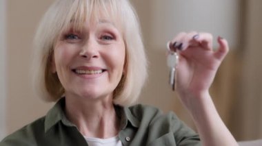 Portrait indoors in new home flat apartment smiling realtor elderly woman showing key from real estate agency service. Happy senior 60s Caucasian lady buying house celebrating moving day relocation