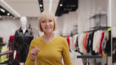 Cheerful active mature professional female saleswoman dancing in clothing store advertises new collection happy woman client rejoices in clothes discounts moves rhythmic to music in fashion boutique