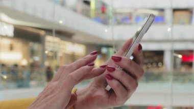 Close-up female manicured hands unrecognizable mature woman holding phone browsing web page communicating in social network using mobile app on smartphone makes order in online store by telephone