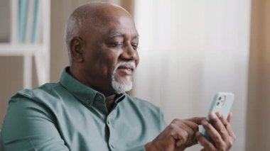 Gri sakallı, kel, yaşlı, yaşlı, yaşlı bir işadamı cep telefonu kullanıyor. İnternette cep telefonu kullanıyor, mobil uygulamadan yemek taksisi sipariş ediyor. Sosyal ağda internet üzerinden mesaj yazıyor.