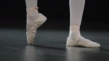 Unrecognizable girl ballerina dancer in pointe shoes for ballet on parquet floor on stage in dance class rehearsing performance does dancing exercise bending toes ankle stretching flexibility position