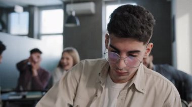 Close-up young depressed student sitting in classroom at desk alone feeling frustrated stress unhappy sad guy nerd suffers from ridicule and bullying from classmates experiencing psychological pain