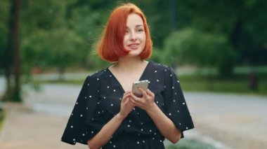 Happy female winner red-haired successful woman girl young model wins online lottery reads positive sms message in mobile phone wins sales discount in internet clothing store rejoices make yes gesture