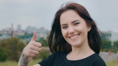 Güzel, gülümseyen esmer kadın model kız, elinde dövmesi olan dışarıda duran şehir manzarası arka planında eğitim servisini tavsiye eden, iyi seçim süper onay jesti.