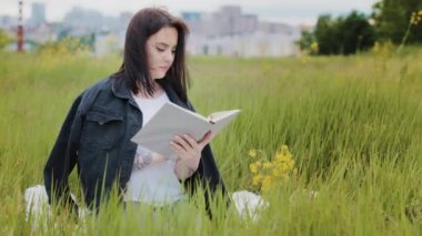 Zeki beyaz kadın açık havada çimenlerde oturur kitap okur edebiyat psikolojisi en çok satan ansiklopedi ders kitabı yeni bir dil öğrenir açık havada sınavlara hazırlanır kültürel rahatlık