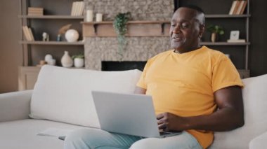African American male senior 50s man working laptop at home talking online to lovely sweetheart shows love gesture with hands folds fingers in heart shape drawing romantic affectionate symbol flirting