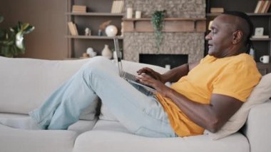 Yaşlı kıdemli Afro-Amerikan işadamı emekli erkek hippi yazar evinde rahat bir kanepede uzanmış internetten internet üzerinden daire alışverişi yaparak interneti tarıyor.