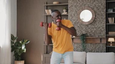 Comical active african athletic sportsman fit strong senior man make gymnastic exercises at home pump muscles biceps domestic workout healthy aerobic sport leisure sing song in dumbbells as microphone