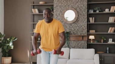 Güçlü atletik formda kıdemli sporcu Afro-Amerikan sağlıklı vücut geliştirici kollarını sallayarak, halterlerle ritmik egzersizler yaparak kasları çalıştırıyor spor ekipmanları kullanarak kasları şişiriyor.
