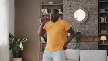 Enerjik erkek kıdemli sporcu Afrikalı Amerikalı olgun emekli sporcu yaşlı aktif dans jimnastiği yapıyor mikrofon gibi en sevdiği şarkıyı halterde söylüyor sağlıklı eğlenceyi sporla birleştiriyor.