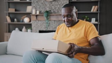 Surprised african adult man unpack parcel box american bachelor homeowner consumer birthday person male buyer get present from internet store delivery shipping open new package feels shock enjoy gift