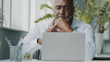 Yaratıcı afrikalı işadamı kıdemli amerikan çalışanı ofiste bilgisayar aygıtı kullanıyor sohbet ediyor iş hakkında düşünüyor çözüm planlıyor zor karar verme stratejisi 