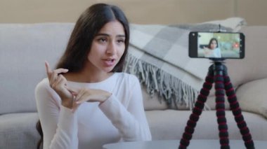 Kadın nüfuzlu blogcu çekici genç bayan tripod kayıtlarında cep telefonu kamerasında evinde oturuyor. Eğitim videoları kişisel yaşam tarzı blog yayınlarını aktarıyor.