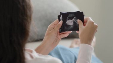 Back view pregnant unrecognizable fertile woman girl future mother wife sitting on sofa at home watching ultrasound pictures of germ child enjoying unborn baby photos ultrasonography medicine service
