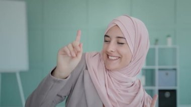 Portrait Islamic happy girl wearing hijab Muslim cheerful woman dancing celebrating victory triumph business winning move hands listening to music makes gesture hey you having fun indoors active dance