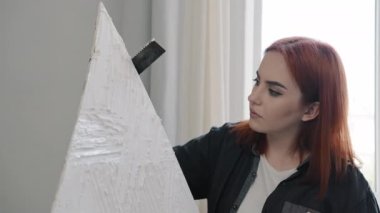 Close up red-haired Caucasian artist decorator creator designer girl 20s woman female painter create picture element of decor draws puts plaster on canvas makes painting drawing decorating modern art