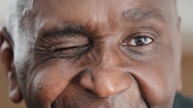 Kısmen erkek, mutlu, siyah gözlerle gülümseyen yaşlı, Afro-Amerikan bir adam. Kırışıklıkları olan yakışıklı, olgun bir vatandaş. Göz kırpıyor, göz kırpıyor. İyi görüyor.