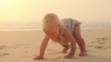 Healthy Caucasian baby toddler crawling on beach to learn to crawl outdoors near sea ocean tropical water. Adorable baby keeping belly and legs down on sand moving funny at seaside sunny day vacation