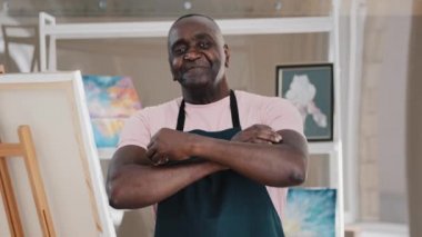 Kapalı portre, mutlu eski 50 'li yılların erkek ressam sanat öğretmeni Afrikalı Amerikalı mutlu yaşlı orta yaşlı sanatçı sanatçı yetenekli tasarımcı silah sanatları stüdyosuna poz verip resim çizmeyi bitiriyor.