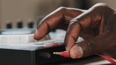 Close-up male hands of unrecognizable African American man DJ musician sound engineer in studio club connects red cord wire power supply in mixer controller prepares to play song recording musical set