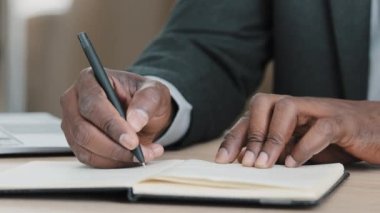 African old senior male hands unrecognizable businessman in formal suit holding pen writing new appointments information in organizer making notes in personal paper planner at desk write in notebook