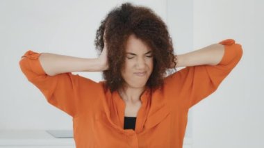 Unhappy stressed African American woman with curly hair covers ears with hands holding head feeling annoyed of noisy loud suffer headache pain confused millennial biracial lady refusing hearing sound